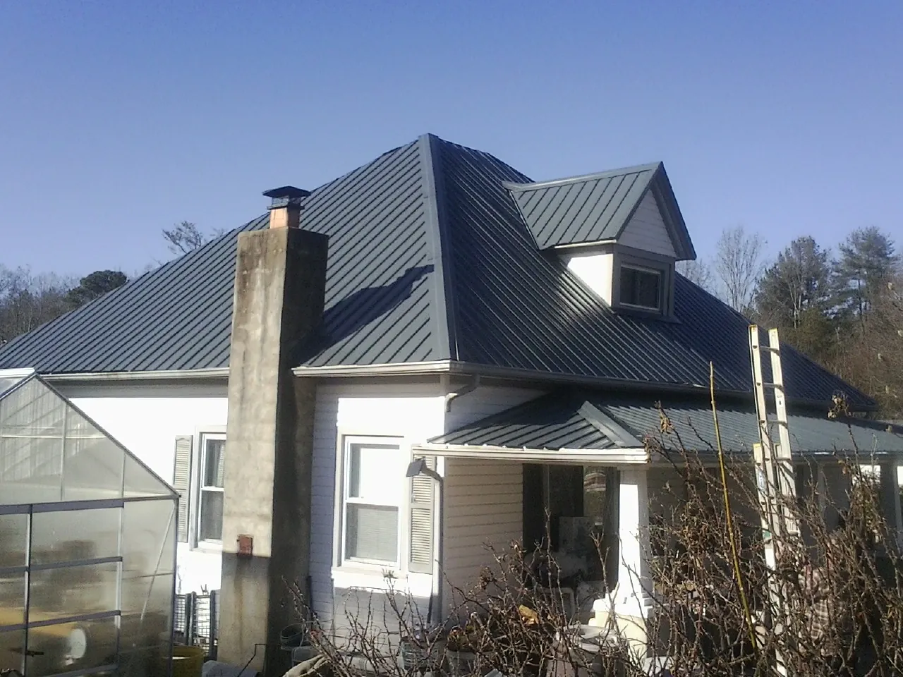 Dark blue standing seam metal roof on a white farmhouse with dormer — Slate & Tile Roof Repair by Roofing Brothers in Malcolm