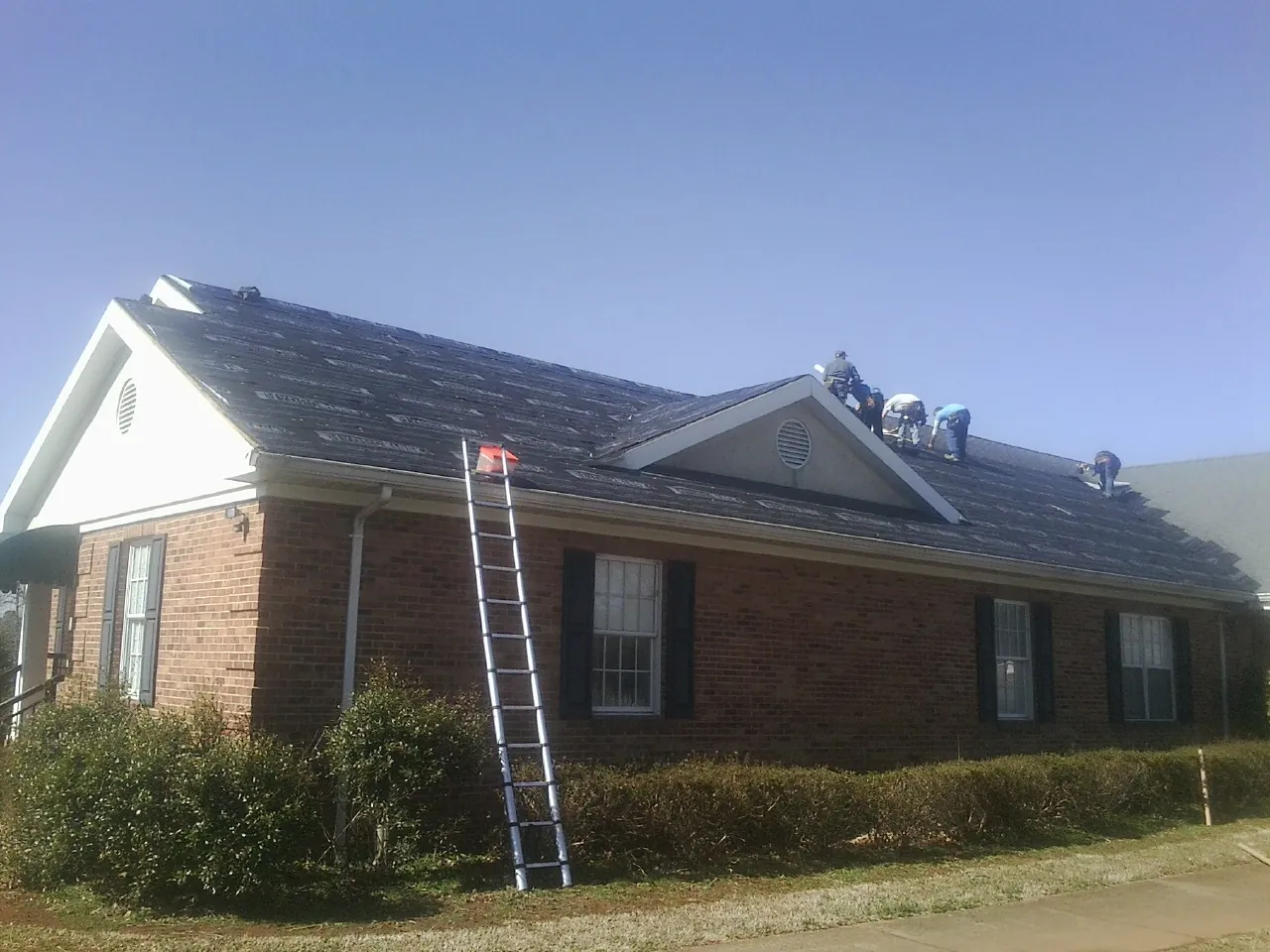 Crew tearing shingles off a brick ranch roof with a ladder set — Metal Roof Repair work by our crew in Malcolm