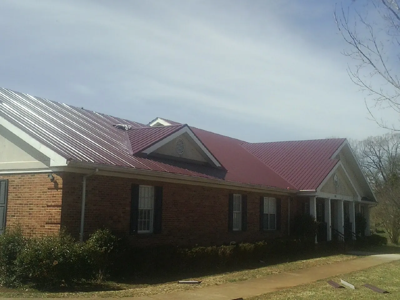 Red metal roof with gabled entries on a long brick building, from a Hail Damage Roof Repair job in Malcolm