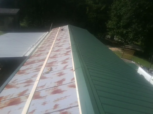 Old rusted panels beside newly installed green metal roofing — Wind Damage Roof Repair by Roofing Brothers in Malcolm