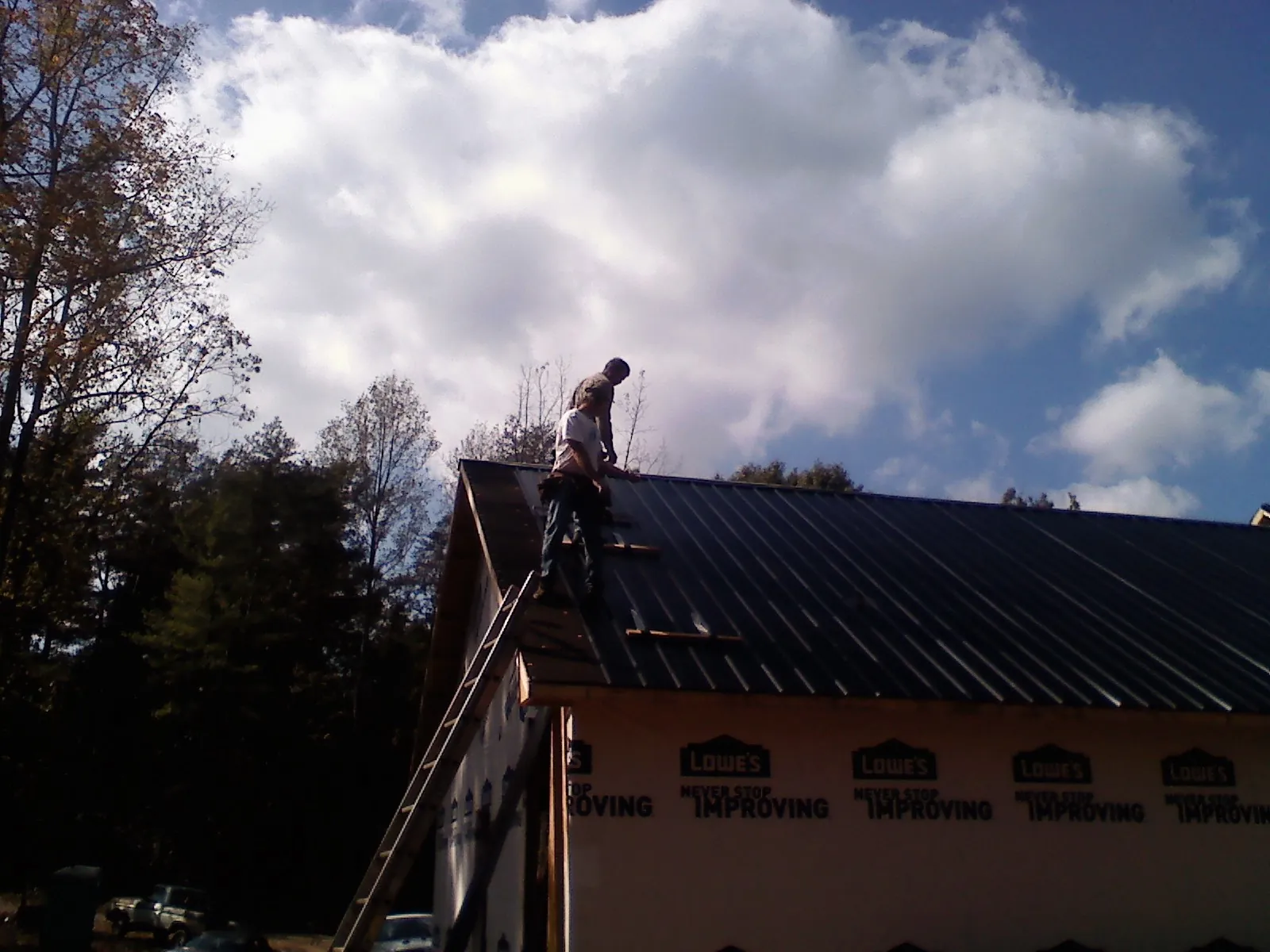 Roofer fastening dark metal panels high against a cloudy sky, from a Roof Inspection job in Malcolm