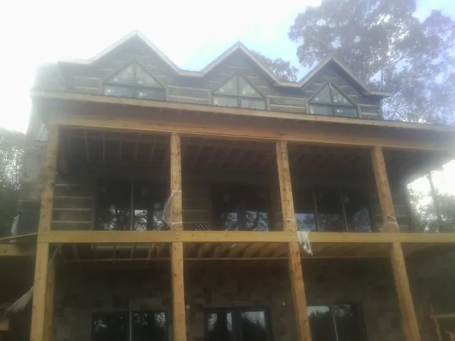 Dormers and porch framing on a large log home under construction — Roof Coating work by our crew in Malcolm