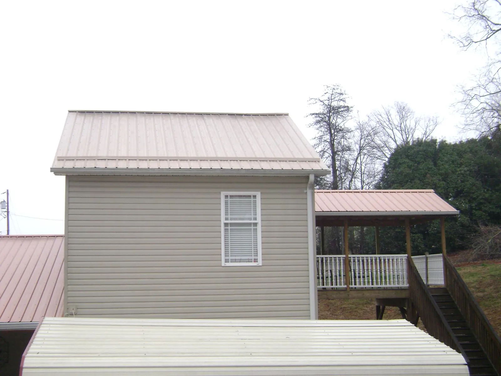 Tan metal roofs on a two story addition and attached porch, from a Roof Replacement job in Malcolm